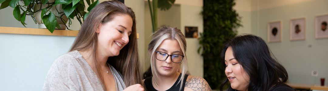 Three women sitting at a coffee shop looking at a computer